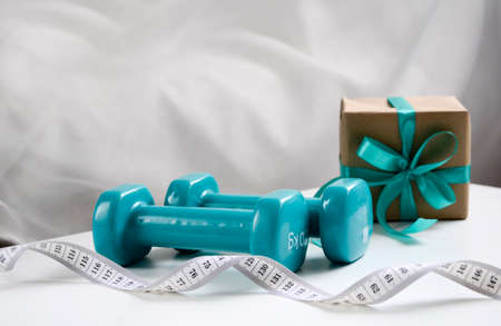 Two sports dumbbells and white measuring tape on white background with copy space, Christmas sport...