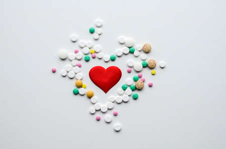 Many different tablets in the shape of heart and red heart on white background. Medical flat lay. Valentine's Day.の写真素材