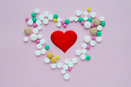 Many different tablets in the shape of heart and red heart on a pink background. Medical flat lay. Valentine's Day.の写真素材