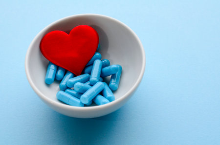 Blue medical capsules in white bowl and a red heart on a blue background. Concept of prevention and treatment of cardiovascular diseases, Valentine's day. Medical flat lay.の写真素材
