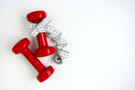 Two red dumbbells, white measuring tape on white background with copy space. Concept of Valentines day, healthy lifestyle, giving gifts, love of sports, shoppingの写真素材
