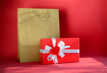 Gift box in shape of heart with bow and craft shopping bag on red background with copy space. Gift for Valentine's Day, March 8, mother's day, birthday.の写真素材