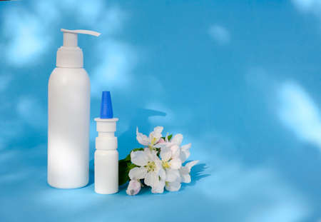 Mock up white cosmetic bottle and spring flowers on blue background with shadows, copy space. Concept of face, body care made from natural plant, cosmetic cream, lotion, shampoo, gel, soap, oil.の写真素材