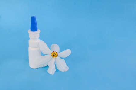 White dropper bottle and spring flowers on blue background with shadows with copy space. Concept of allergy treatment. Nose drops or spray for allergies, rhinitis.の写真素材