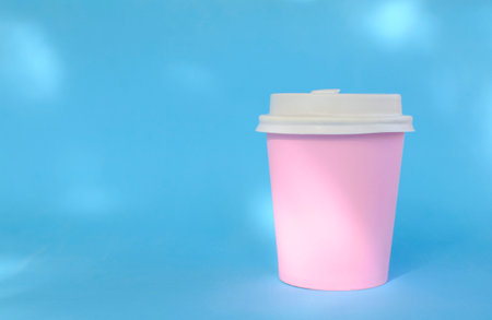 Pink paper coffee cup closed with white lid on blue background with shadows. natural eco packaging.の写真素材
