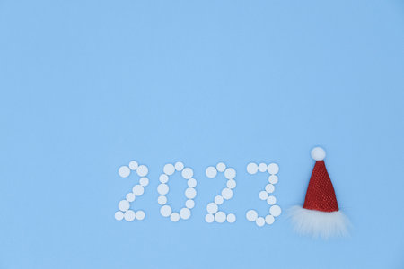 White medical pills in form of number 2023 and Santa hat on blue background with copy space....