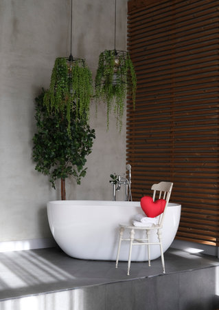 Modern bathroom interior design with concrete walls, wooden slats and white bathtub.vintage chair with towels and heart. Valentine's day concept, relaxation, massage, gifts, care, rest.の写真素材