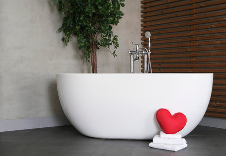 Modern bathroom interior design with concrete walls, wooden slats and white bathtub, green plants. towels and heart. Valentine's day concept, relaxation, massage, gifts, care, rest.の写真素材