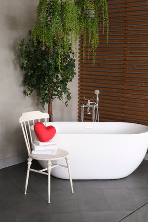 Modern bathroom interior design with concrete walls, wooden slats and white bathtub.vintage chair with towels and heart. Valentine's day concept, relaxation, massage, gifts, care, rest.の写真素材