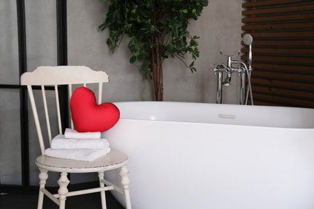 Modern bathroom interior design with concrete walls, wooden slats and white bathtub.vintage chair with towels and heart. Valentine's day concept, relaxation, massage, gifts, care, rest. Close up.の写真素材