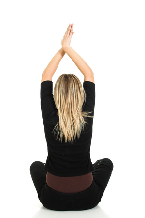 Young beautiful blond girl sitting and holding hands up isolated on white backgroundの写真素材