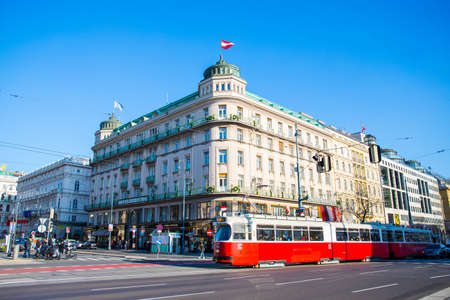 Outdoor scene of Vienna Streets ( Austria ) with people walking, the traditional red tram and Austrian flag next to the Opera on a sunny dayのeditorial素材