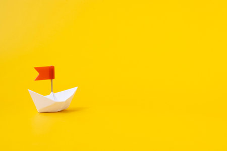White paper boat with a red flag on a yellow background. The concept of success and development. Business.の写真素材