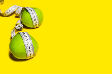 Green apples wrapped with a measuring tape on a yellow background. Diet concept.の写真素材