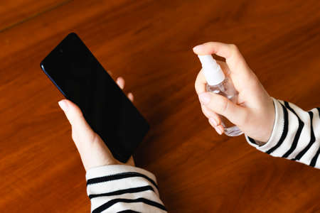 Disinfection of the smartphone screen with a disinfectant. Smartphone and disinfectant in a female hand.の写真素材