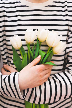 A bouquet of white tulips in hands on a background in the form of horizontal white stripes. Concept.の写真素材