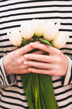 A bouquet of white tulips in hands on a background in the form of horizontal white stripes. Flowers of white tulips.の写真素材