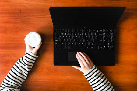 Laptop, coffee and female hands. Wooden table in the office. Remote work at home. Office workplace.の写真素材