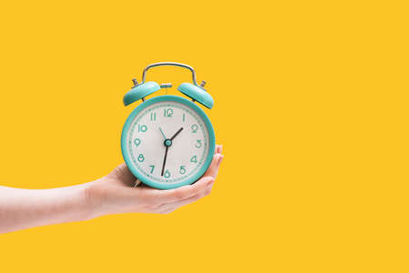 Alarm clock. Vintage watch in a female hand on a yellow background.