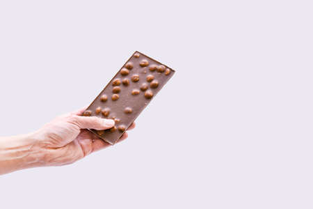 Chocolate with nuts. Male hand holds a bar of chocolate on a gray background.