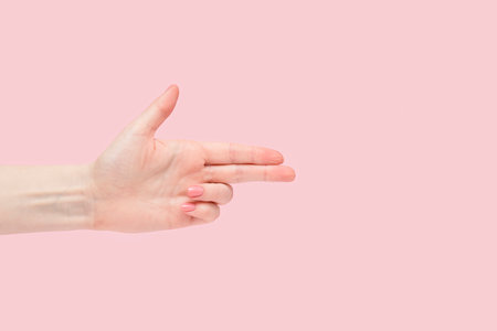 Finger gun. Pointing gesture with a female hand on a pink background.