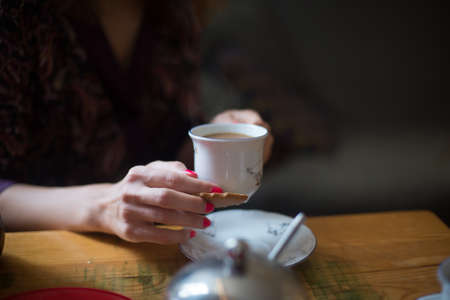 Close-up of a woman's hands holding a cup of coffee and cookies in a coffee shop on a wooden table background.の写真素材