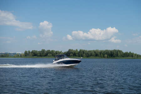 A motor boat cruises on the water against the background of an island overgrown with green trees.