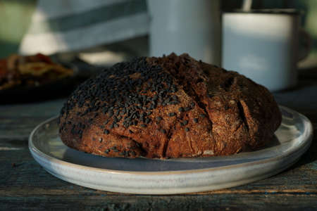 Round homemade bread, sprinkled with black sesame seeds, on a white ceramic plate. Homemade...