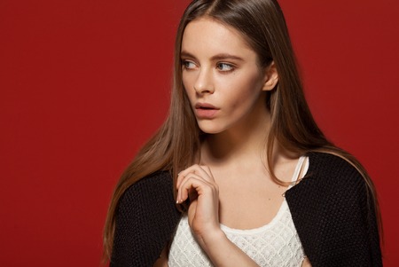 Woman beautiful face portrait. Skin care style face hand touching. Female model studio posing. Red background. Fashion shot.の写真素材