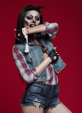 Closeup portrait of one beautiful wild young woman with bright golden animal makeup with thorns on face ion red background, horizontal picture. Halloween concept.の写真素材