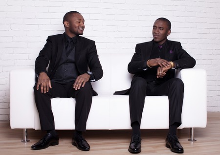 two happy african man businessmen in black suit on white sofaの写真素材