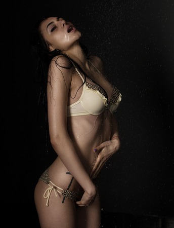 Happy young beautiful full body brunette woman posing in modern bikini swim suite with windy hair on a black backgroundの写真素材