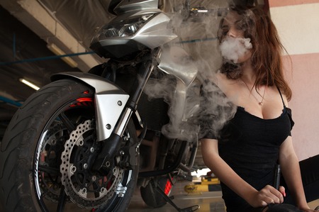 Young beautiful woman smoking ( vaping ) e-cigarette with smoke