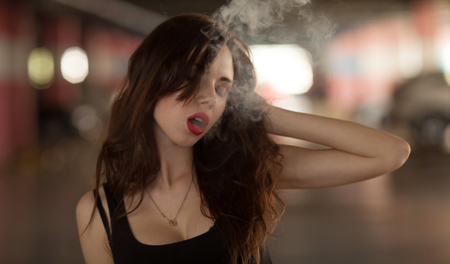 Young beautiful woman smoking ( vaping ) e-cigarette with smokeの写真素材
