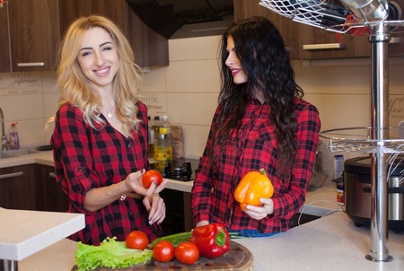 Two sexy woman blond and brunette in red shirt cooking on kitchen. Blurred background.の写真素材