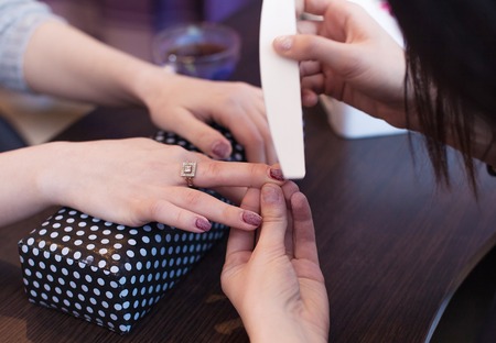 Closeup shot of a woman in a nail salon receiving a manicure by a beautician with nail file. Woman getting nail manicure. Beautician file nails to a customer. Blurred backgroundの写真素材