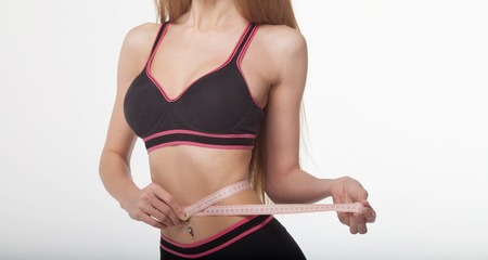 Fit and healthy young lady measuring her waist with a tape measure in centimeters and millimeters