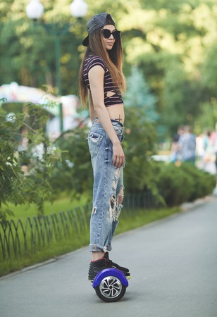 Feet of girl in jeans riding electric mini hover board scooter outdoors in park. Ecological city...