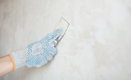 Man hand. Closeup of palette-knife or scraper and cement filling for house renovation construction.の写真素材