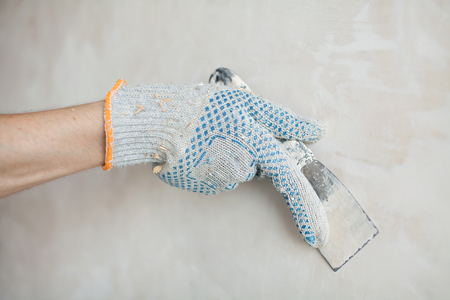 Man hand. Closeup of palette-knife or scraper and cement filling for house renovation construction.の写真素材