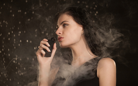 Young beautiful woman vaping e-cigarette. Water flowing on woman face.の写真素材