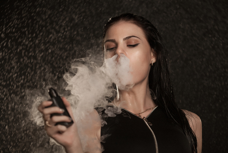 Young beautiful woman vaping e-cigarette. Water flowing on woman face.