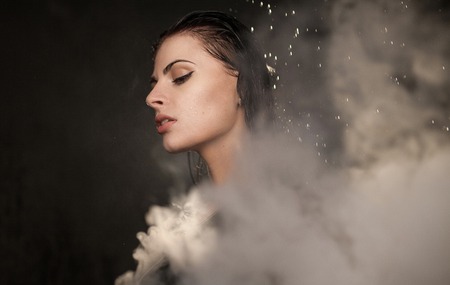 Young beautiful woman vaping e-cigarette. Water flowing on woman face.の写真素材