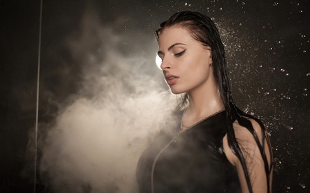 Young beautiful woman vaping e-cigarette. Water flowing on woman face.の写真素材