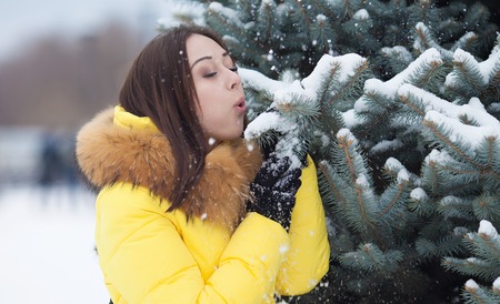 Happy beautiful young woman blowing snowflakes from her hands in a winter dayの写真素材