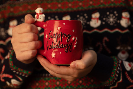 Merry Christmas and Happy New Year. Close-up of female hands holding a red mug with lettering.の写真素材
