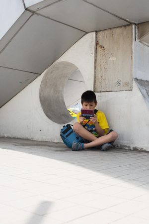 BANGKOK, THAILAND-FEBRUARY 7,2016 : Unidentified boy play games press is living under a bridge Tourists come to visit Bangkok art and culture center at Pathumwan junction, Bangkok art and cultural center is the first modern art center in Thailand, Feb 7 2のeditorial素材