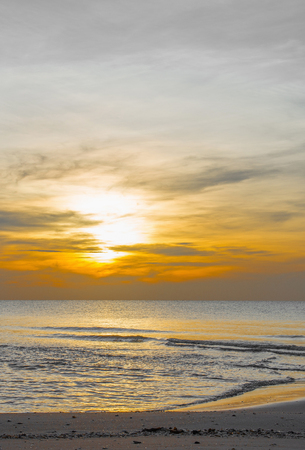 Sun sets over horizon of ocean. Sky, water and shore in the evening painted in orange, gold color.の写真素材