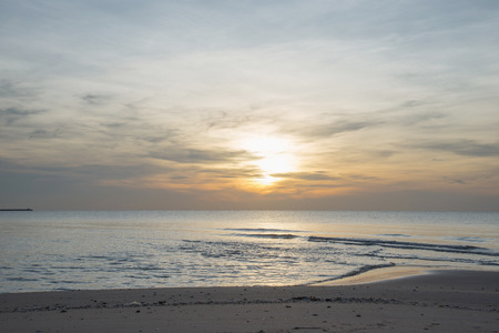 Sun sets over horizon of ocean. Sky, water and shore in the evening painted in orange, gold color.の写真素材
