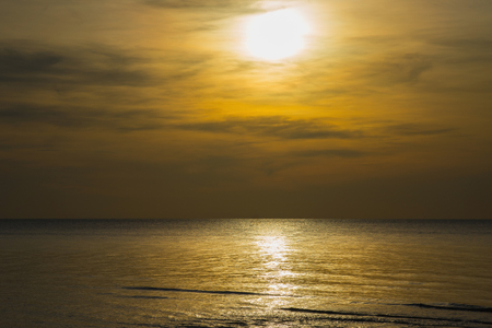 Sun sets over horizon of ocean. Sky, water and shore in the evening painted in orange, gold color.の写真素材